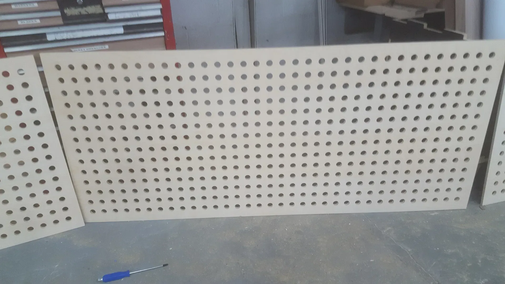 A batch of freshly fabricated, high-quality wooden pegboard panels sitting in our shop. These panels are precision-drilled for optimal strength and modular organization, serving as a clean, versatile base for our custom tool storage solutions. These pieces are ready for finishing touches and installation, reflecting the clean, functional design aesthetic we integrate into our workshop organization projects.