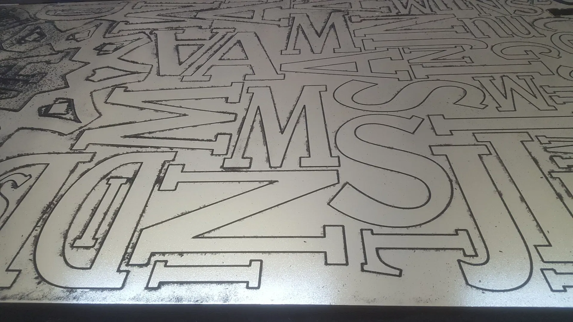 This image displays a large metal sheet currently undergoing the laser cutting process. It shows a series of interlocking, custom-designed alphabetic characters precisely etched into the surface. The high-contrast outlines clearly demonstrate the precision and efficiency of our CNC laser cutting machinery, highlighting our capability to maximize material yield by nesting multiple custom parts on a single sheet of metal. This project showcases the clean, professional results we deliver for signage and industrial branding clients.