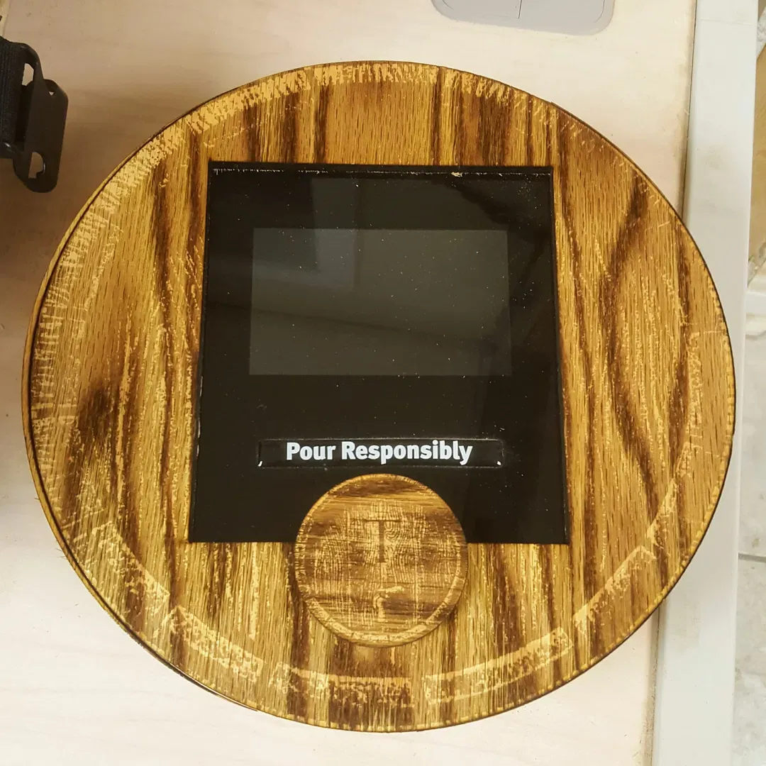 A top-down view of a circular, wood-grain digital tap handle display. The unit features a black LCD screen for branding or pour information and a prominently etched "Pour Responsibly" label. The center circular inlay displays a small logo, highlighting our focus on merging traditional aesthetics with smart pouring technology for modern bar environments.
